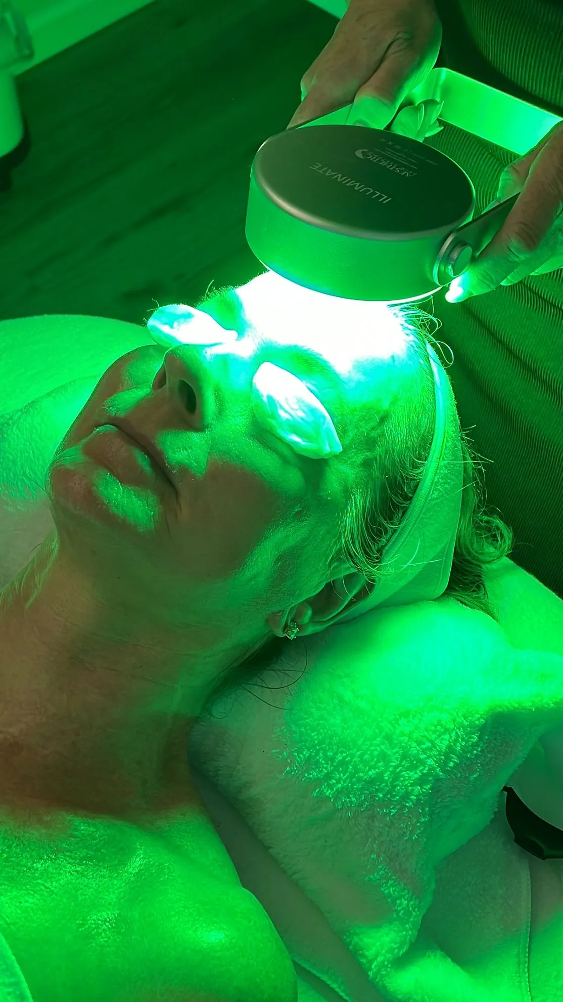 A woman is getting a green light treatment on her face.