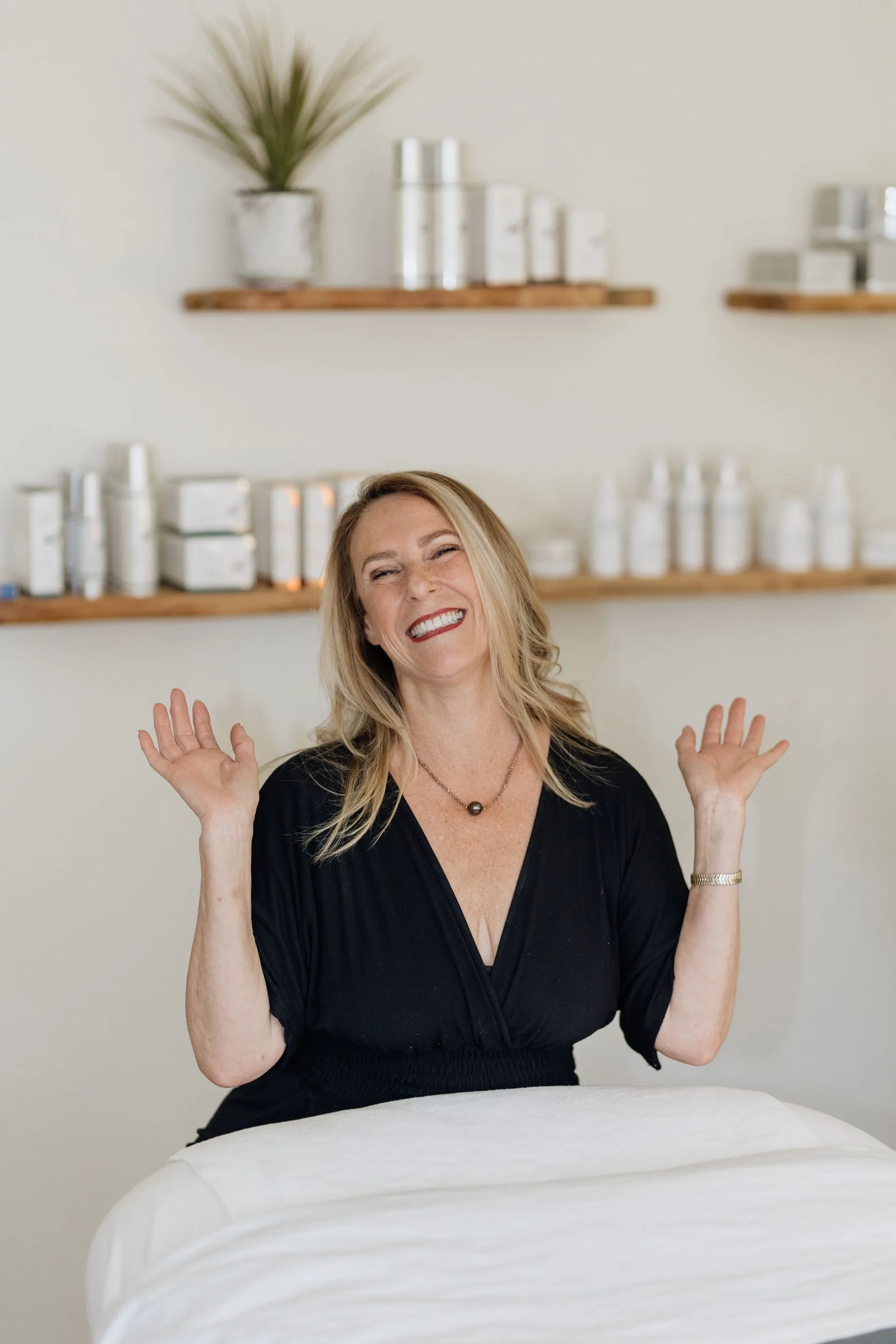 A woman in a black dress is sitting at a table with her arms outstretched.